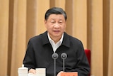 a man in a simple black jacket sits behind microphones