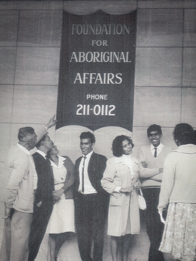 A group of young adults stand underneath a sign 'Foundation for Aboriginal Affairs'