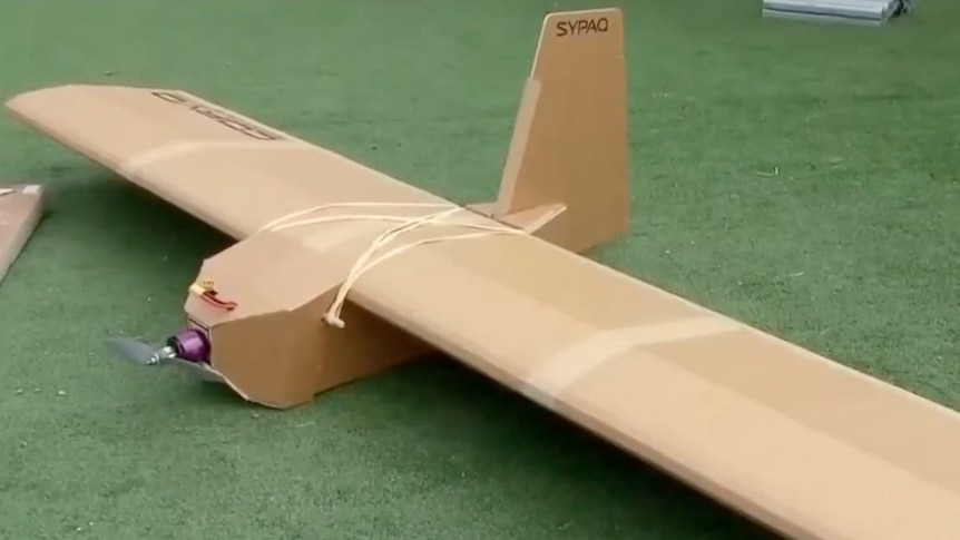  A cardboard drone that looks like a tiny plane rests on AstroTurf. 