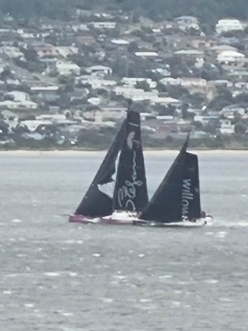 Two yachts, once with a torn mainsail, side by side in a river.