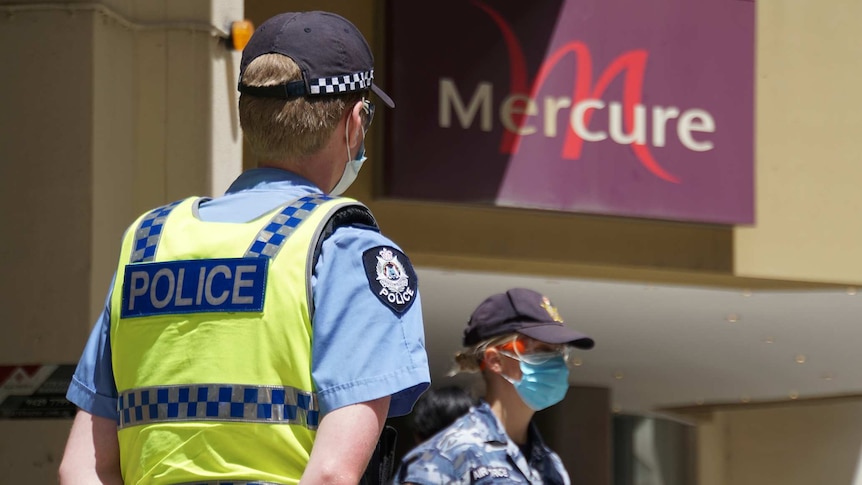 A police officer and an Australian Border Force officer stand wearing face masks outside the Mercure Hotel in Perth.