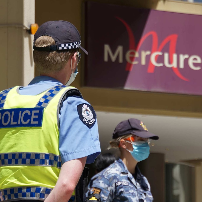 A police officer and an Australian Border Force officer stand wearing face masks outside the Mercure Hotel in Perth.