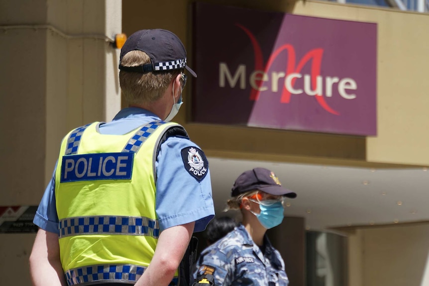 A police officer and an Australian Border Force officer stand wearing face masks outside the Mercure Hotel in Perth.