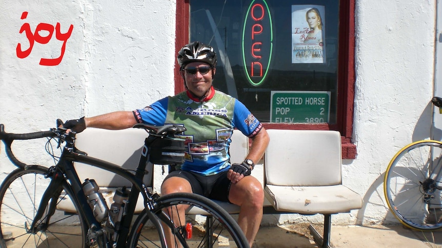 Jonathan Page sits next to his bicycle while smiling.