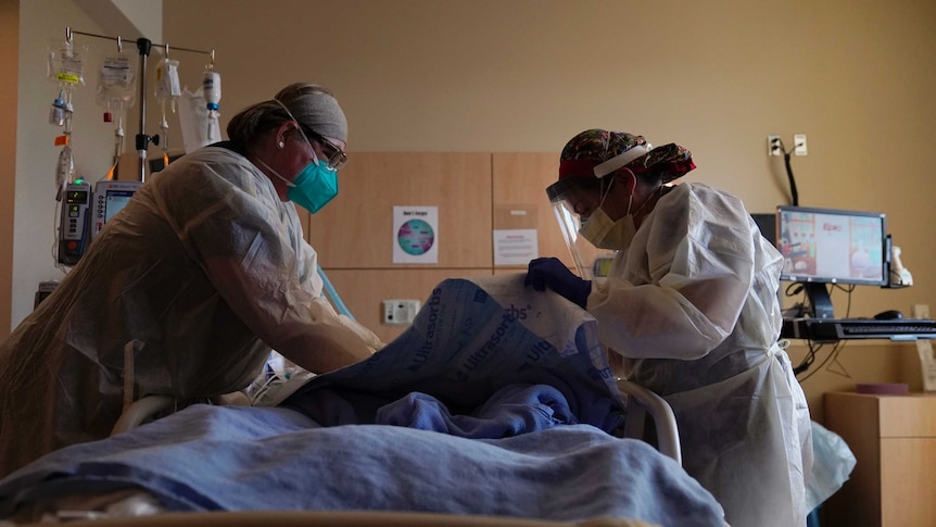 Two nurses treat a COVID patient laying in a hospital bed.