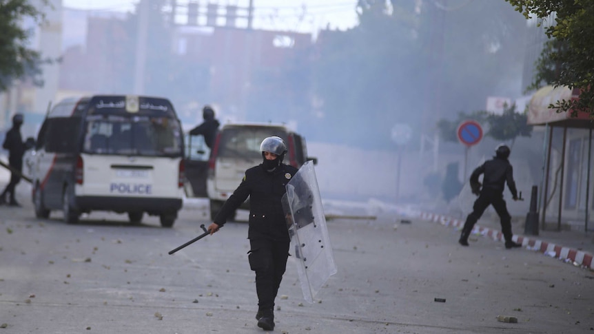 Riot policemen walk on a road amid tear gas during a protest in Kasserine.