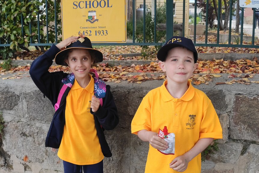 Two kids in yellow school uniform outside a gate.