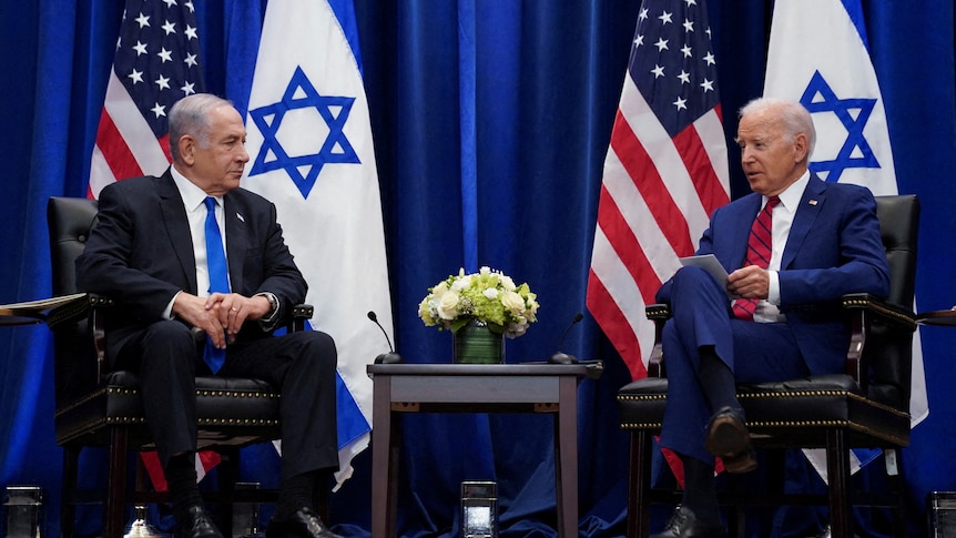Israel Prime Minister Benjamin Netanyahu and US President Joe Biden talk while sitting on stage in front of their flags.