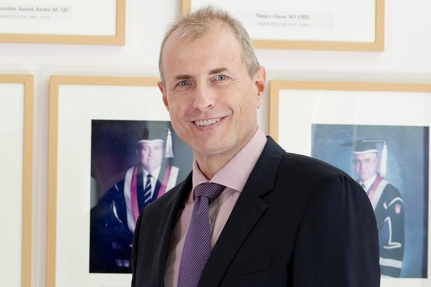 Paul Henderson standing smiling in a room filled with pictures of former chancellors.