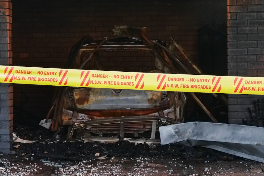 A burnt out car with red and yellow tape in front of it reading 'danger no entry NSW fire brigades'