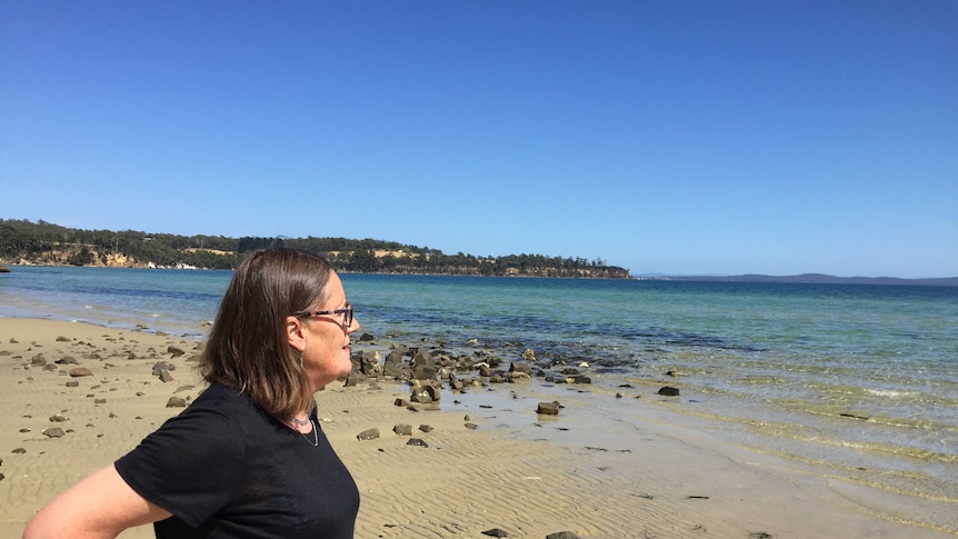 woman looks out at blue water in tasmanian beach with yellow sand