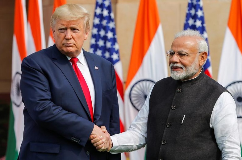 Donald Trump shacjing hands with Narendra Modi in front of  US and Indian flags.