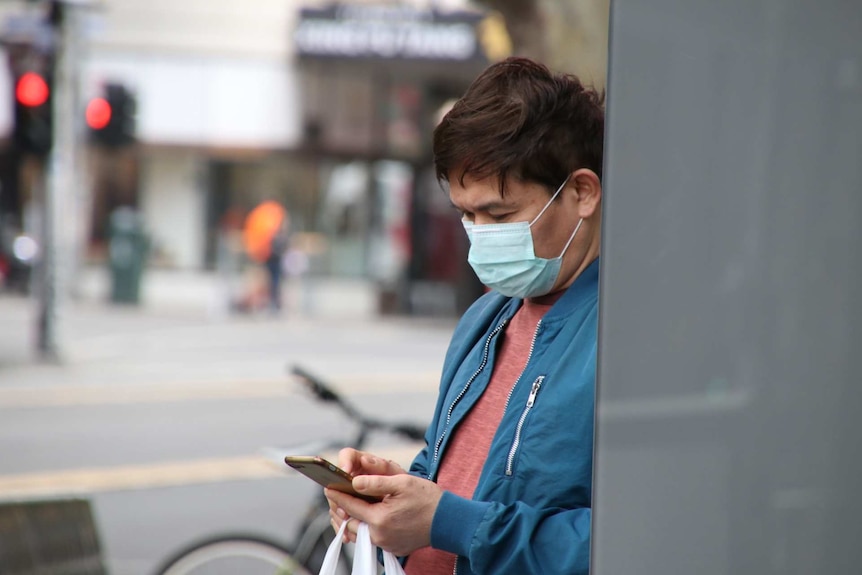 A man wearing a surgical mask looks down at his phone