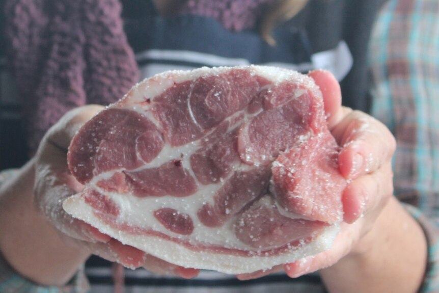 Hands holding a cut of pork.