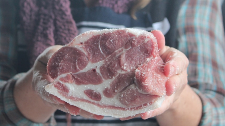 Hands holding a cut of pork.