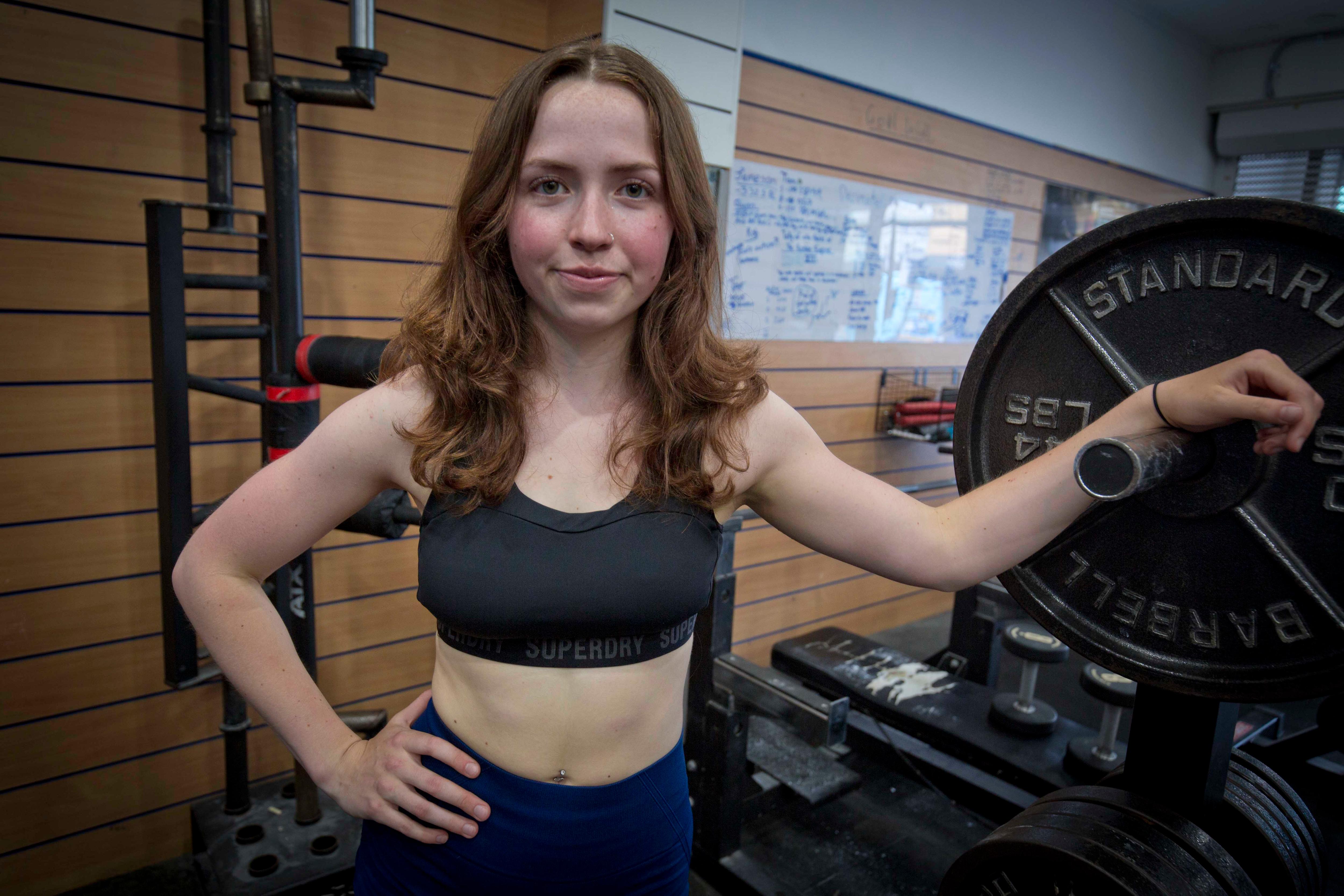 Talulla Clarkson wears gym gear while leaning against a rack of weights