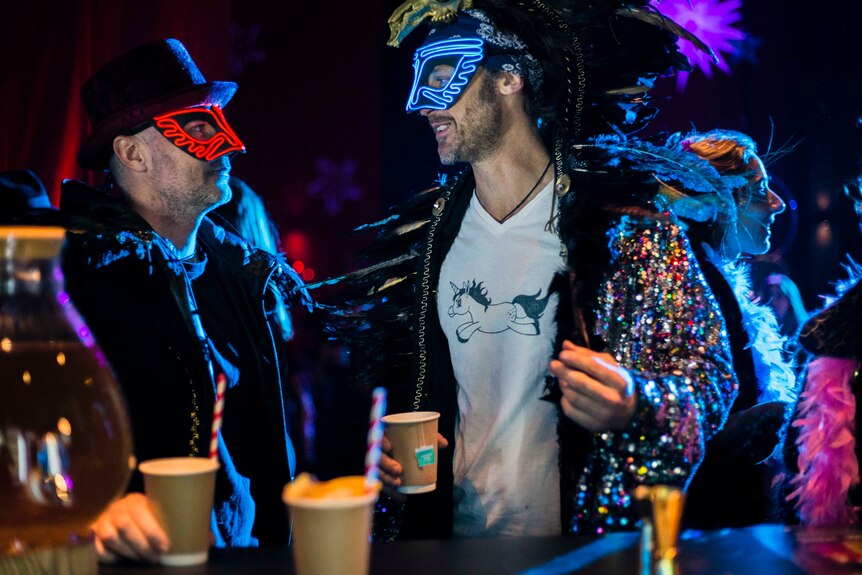 two men in glowing masks at a bar holding cups