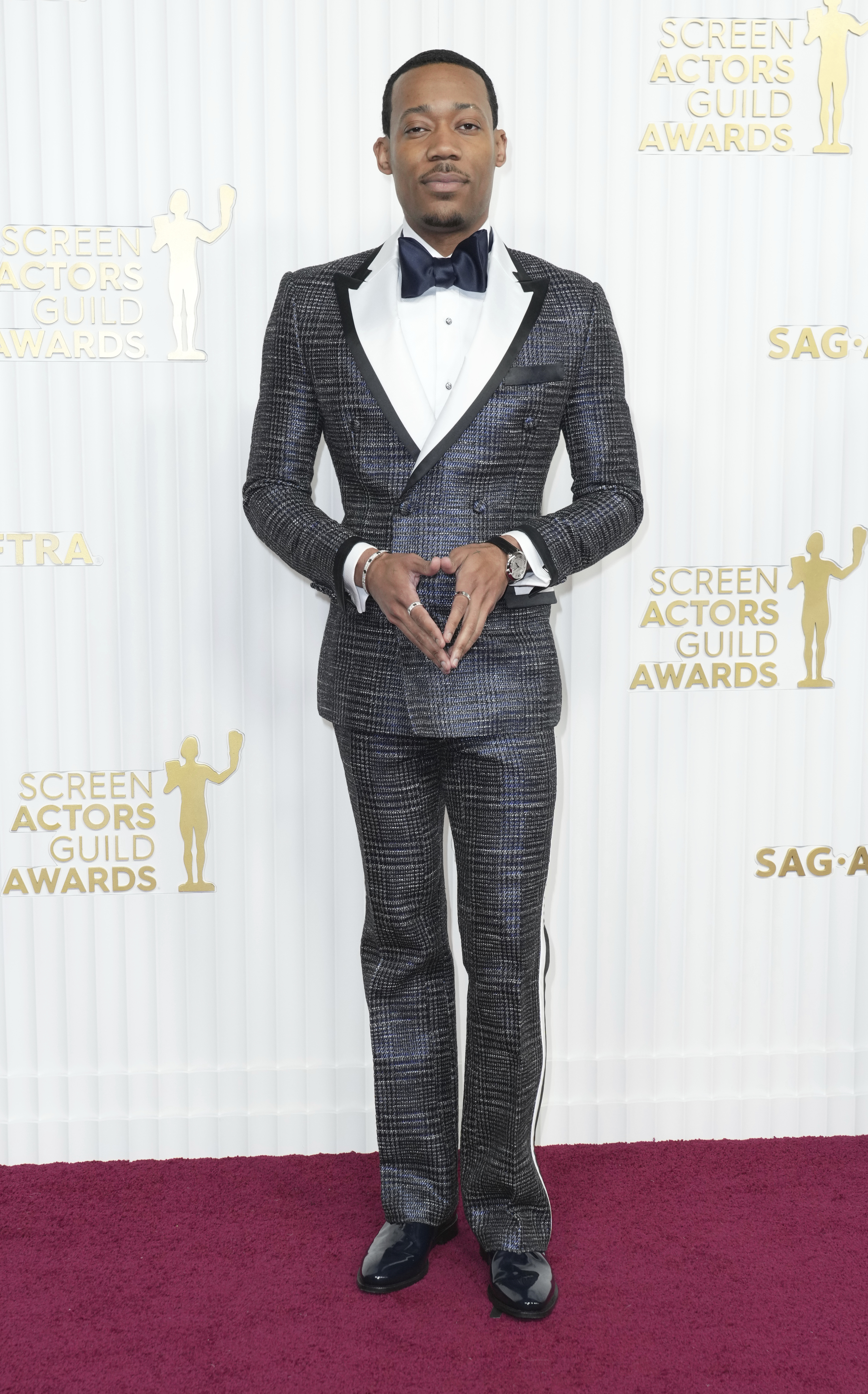 Tyler James Williams wearing a dark blue tweed-like suit with a dark blue bow tie 