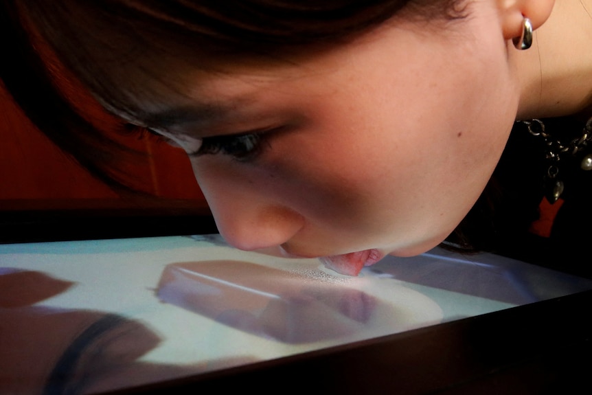 A demonstrator licks the screen of a prototype lickable TV screen that can imitate the flavours of various foods.