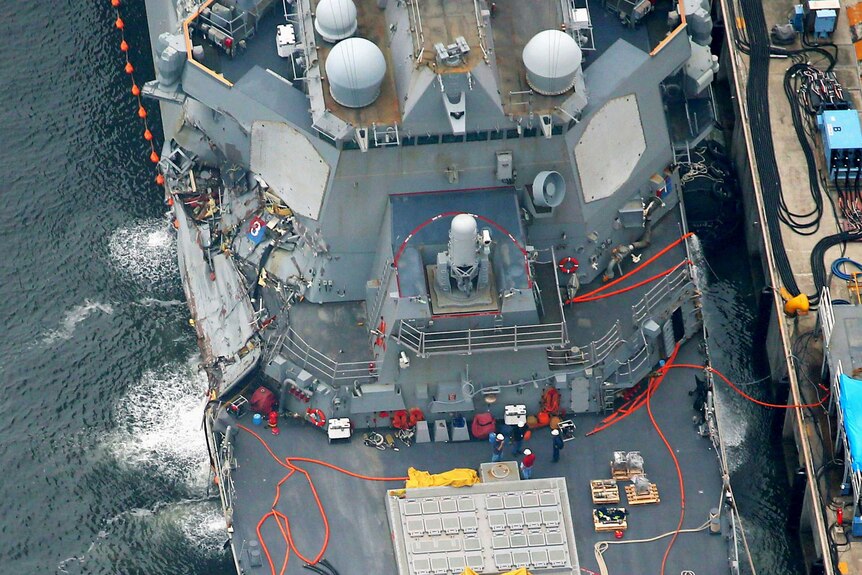 The damaged USS Fitzgerald, a missile destroyer, is seen from above. Significant damage to the ship's starboard side is visible.