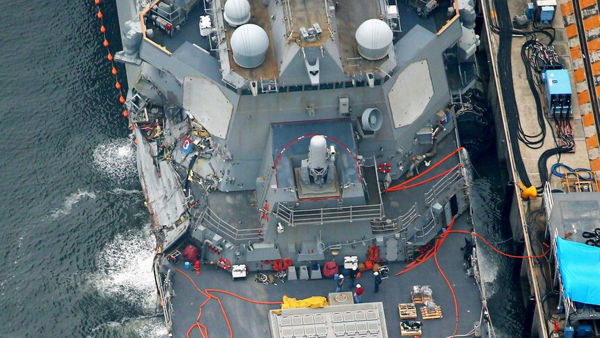The damaged USS Fitzgerald, a missile destroyer, is seen from above. Significant damage to the ship's starboard side is visible.