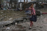 A Palestinian girl carries a blankets as she walks past the site of a deadly explosion