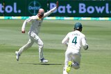 An Australian bowler runs away, his arm raised in triumph, after taking an Ashes wicket as the wicketkeeper runs toward him.