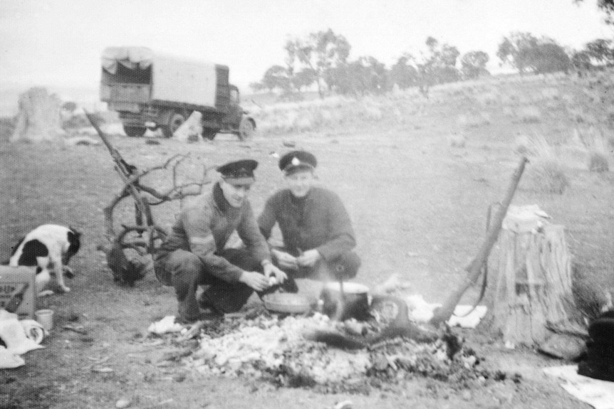 Two RAAF personnel on guard duty at the crash site of the RAAF Lockheed Hudson preparing breakfast over the remains of a bonfire