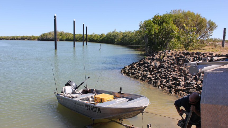 A man hitching a boat to a trailer at a boat ramp surrounded by blue green river water.