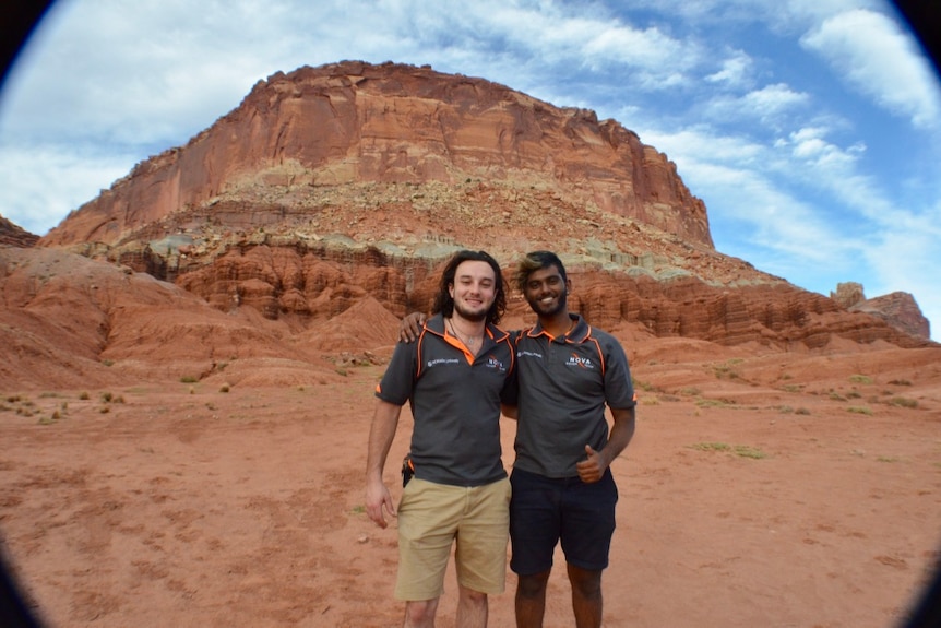 Two men stand in front of rock formations
