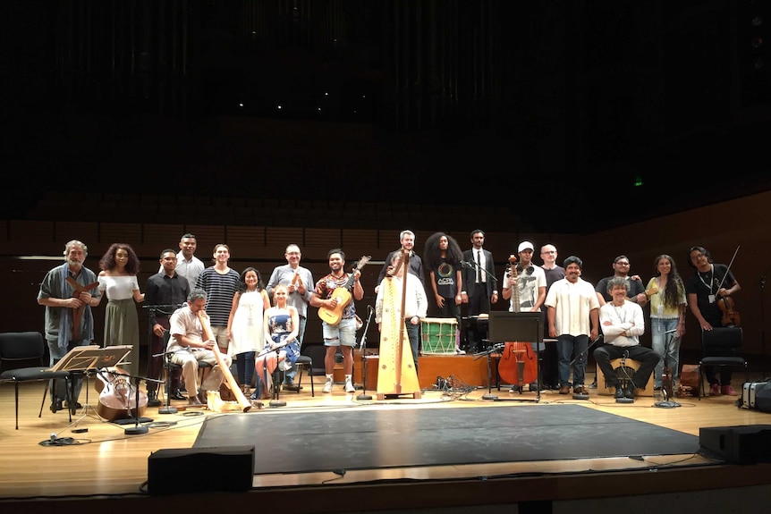 Jordi Savall standing on the QPAC stage with the combined ensembles in a line, smiling at the camera.