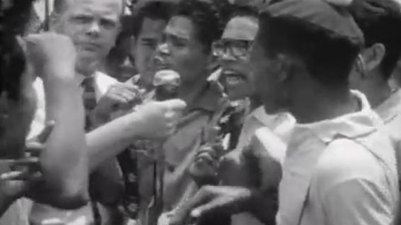 Indonesian man speaks into microphone while surrounded by crowd