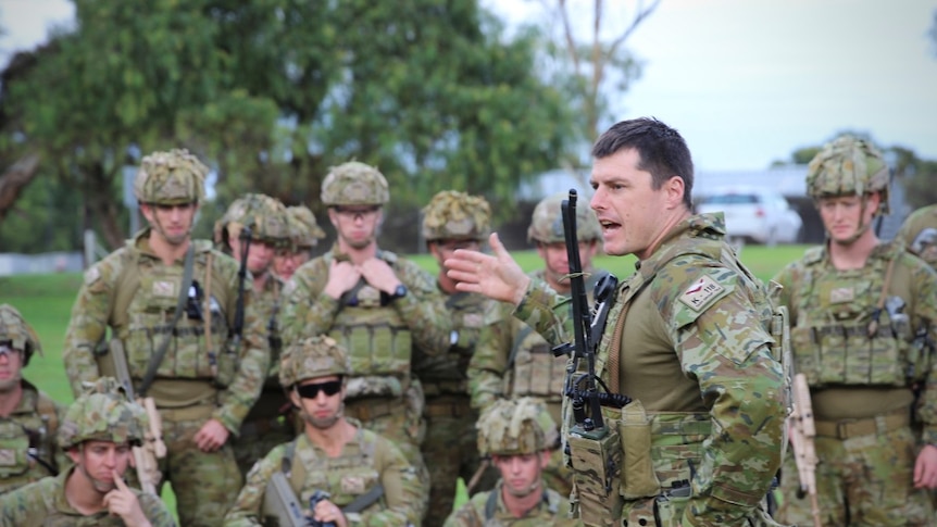 An Australian Army major gives orders to his soldiers who are assembled outside in full combat gear