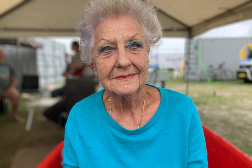 An older woman with grey hair and a blue T-shirt looks into the camera.