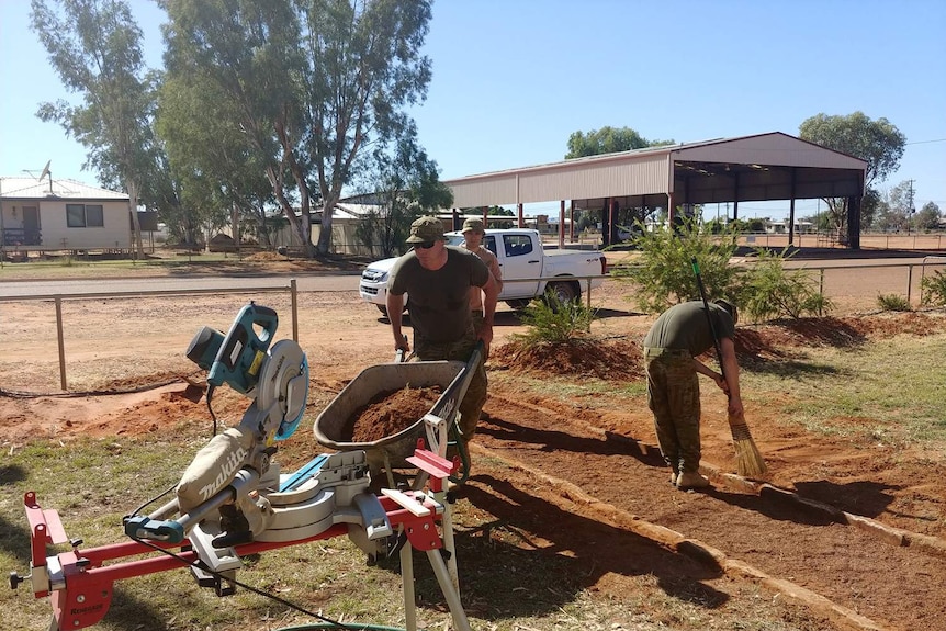 Three ADF men in army fatigues pushing a wheelbarrow and fixing the church path