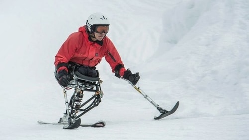 Hari Budha Magar in a red ski jacket skiing in snow using a seat like single ski and two smaller hand held skiis on poles
