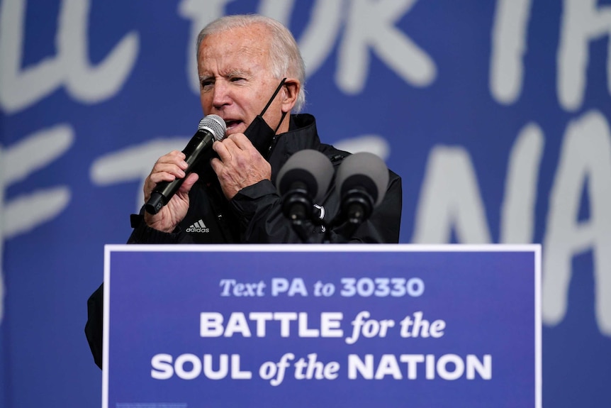 Joe Biden lowers his black face mask to speak into a microphone