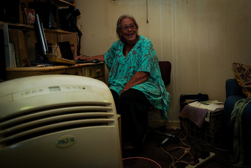 A woman smiles while sitting in her home, with an AC unit in the foreground