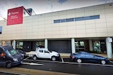 cars parked beside a hospital entrance with others driving past on the road