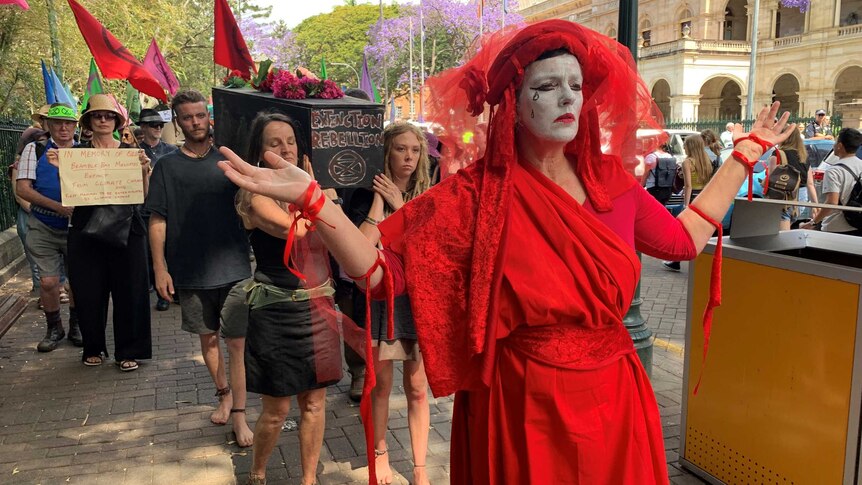 A woman in red with tears on her face and a group of people carrying a coffin.