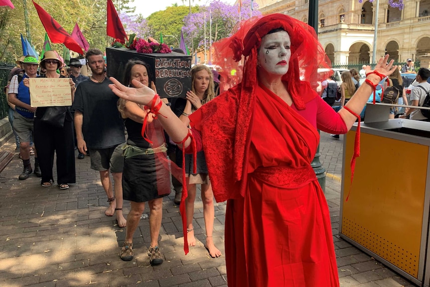 A woman in red with tears on her face and a group of people carrying a coffin.