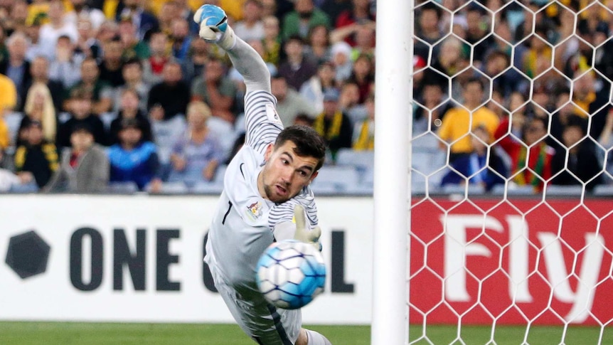 Socceroos keeper Mat Ryan dives at a ball that hit the post from a Syria free kick
