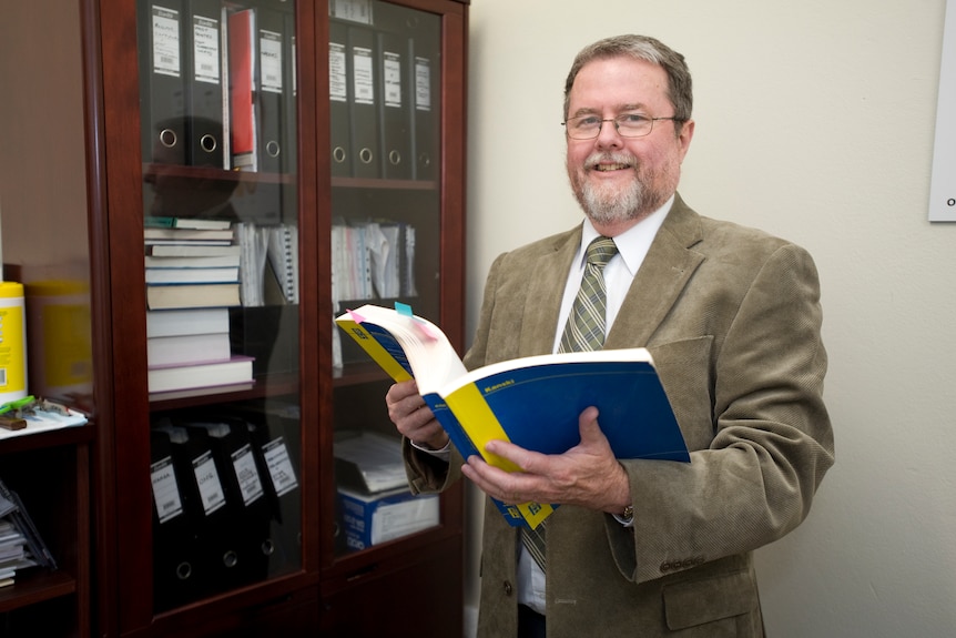 A man holding a book smiles at the camera 