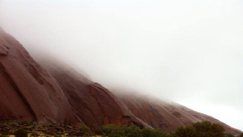 One side of Uluru with fog hanging over the top of it