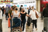 A group of people walk out of the airport, all wearing masks.