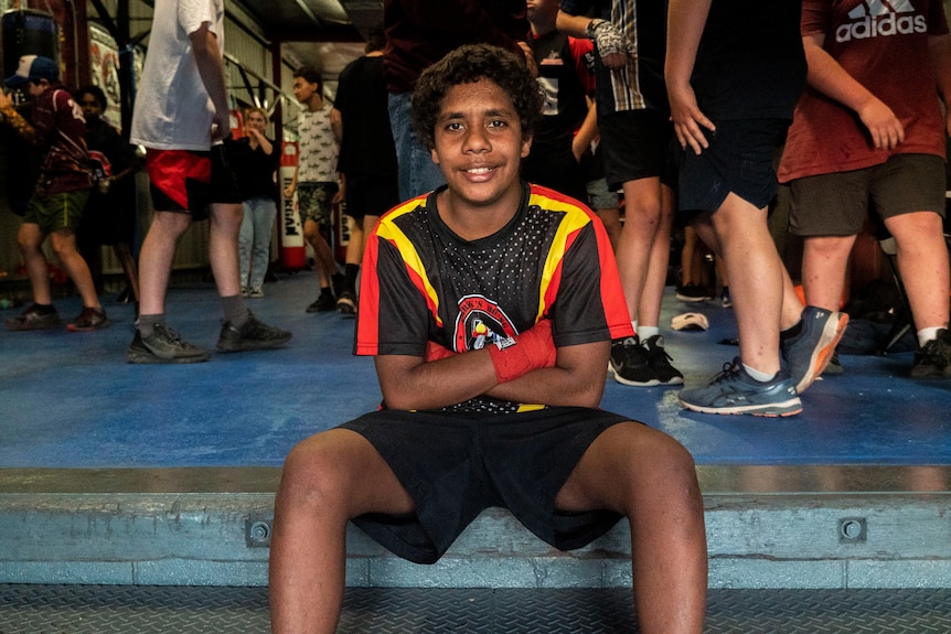 Young Indigenous boxer sits on steps with his arms crossed. 