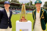 Wearing whites and blazers, Heather Knight and Meg Lanning flank a trophy