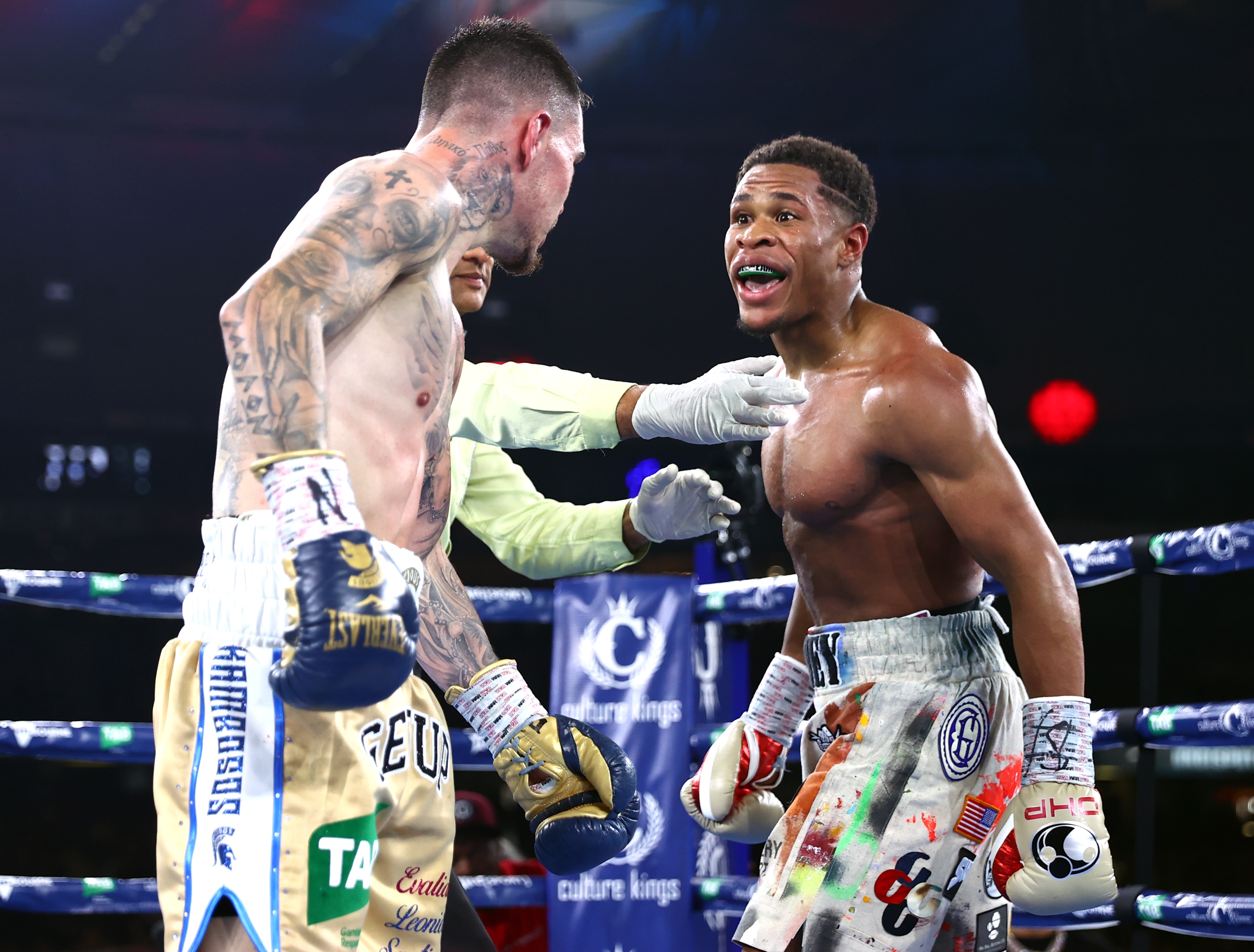 Devin Haney leans forward and makes a face at George Kambosos as a referee puts his arm between them 