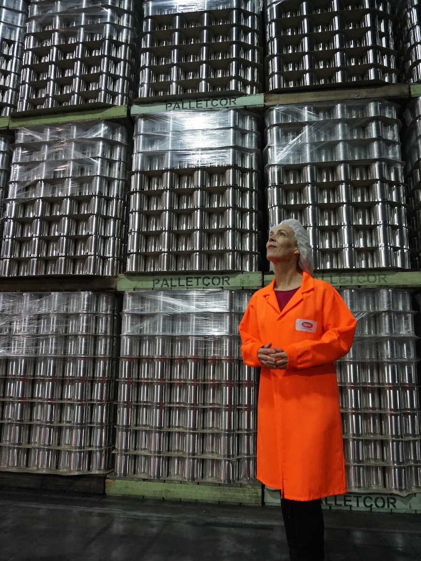 A woman in an orange jumpsuit is dwarfed by a stack of pallets of tinned baked beans.