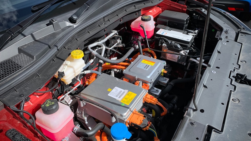 The hood of a red electric vehicle is popped, showing the internal engine